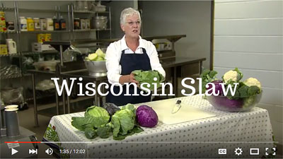 Preview of the Wisconsin Slaw video featuring a woman in a black apron holding a cabbage over a cutting board