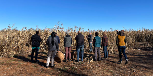 A group of ten people standing in front of a corn field that is ready to harvest.