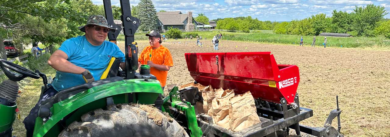 A man sitting on a tractor parked in front of a small group of people working in a plowed field