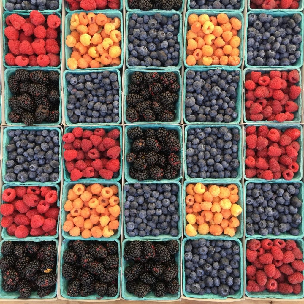 Blueberries, raspberries, cherries, and blackberries are displayed in green pint-sized containers.