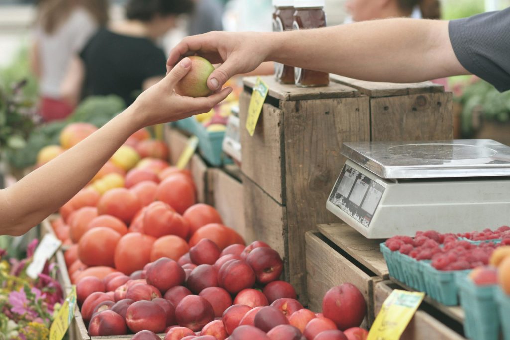 A vendor hands an apple to a customer at a farmers market stand