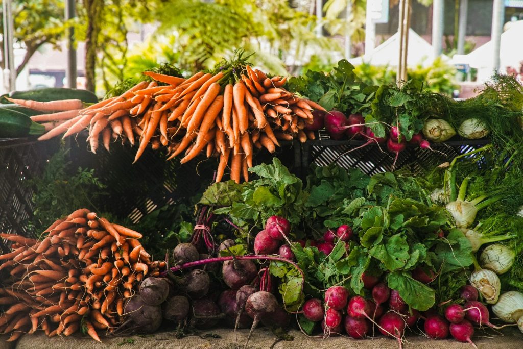 Carrots, beets, and assorted root vegetables are displayed at a farmers market stand.
